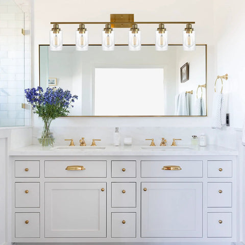 Modern bathroom with gold fixture, wide mirror, and elegant white vanity with decorative hardware and floral accent
