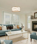 Gold Drum Pendant Chandelier Light Fixture with White Fabric Shade hanging in a modern living room above a marble coffee table.