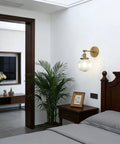 Vintage Industrial Wall Sconce Lighting Fixture With Five Point Nine Inch Round Clear Ribbed Glass Globe Antique Brass Gold Finish E26 Base 60W Max 110-120V Dimmable With LED CFL Halogen Incandescent Bulbs Hallway Living Room mounted above a bedroom nightstand.