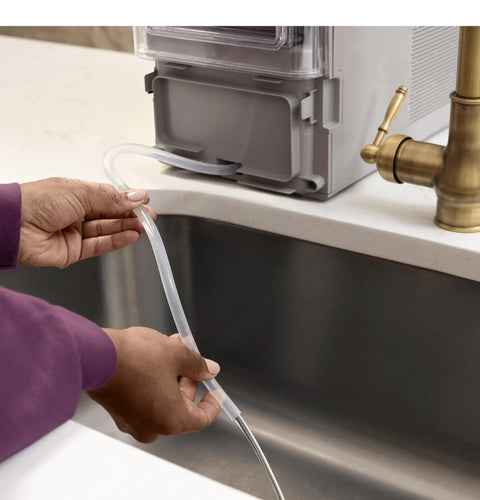 Hand holding water line connected to the Legit Nugget Ice Maker, Portable Countertop Pellet Ice Machine, Stone Grey.