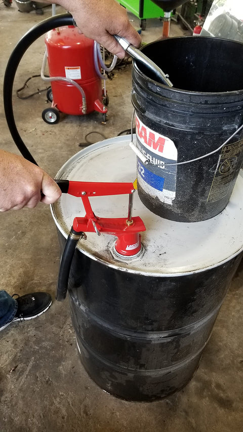 Person using Lincoln 1335 Lever Action Fluid Transfer Pump on 55-gallon drum, with removable hose and brass rings, visible in workspace.