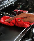 Hand using red Beefy 50 Pack Shop Towels 14x12 for automotive cleaning, showing 100% cotton towel on car engine