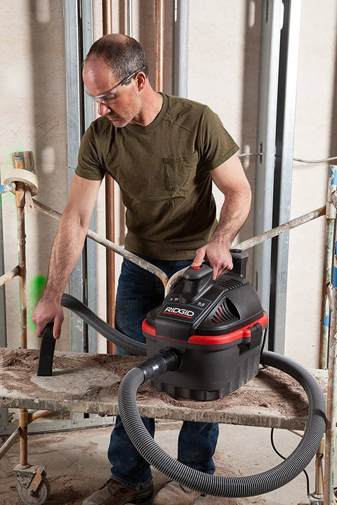 Person using 4-Gallon Portable Wet And Dry Vacuum Cleaner With A 5.0 Peak HP Motor on a jobsite, featuring grab-and-go lightweight design.