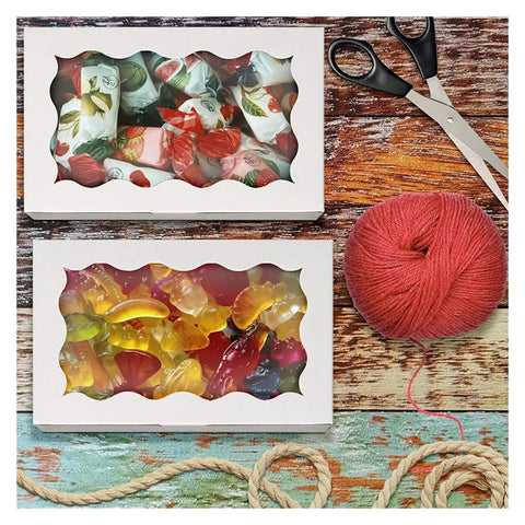 20 Pcs Kraft Paper Gift Boxes With Window showing candies, placed with scissors and yarn on a wooden surface.