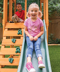 Children playing on weatherproof wooden swing set with slide and rock wall, durable pre-treated lumber for outdoor playset.