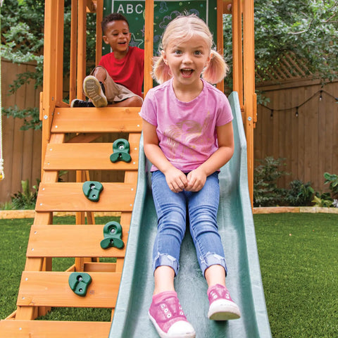 Children playing on weatherproof wooden swing set with slide and rock wall, durable pre-treated lumber for outdoor playset.