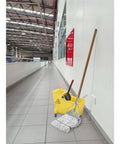Industrial Grade 59 Inch Quick Change Mop Stick With Wooden Handle And Steelhead beside yellow bucket in hallway