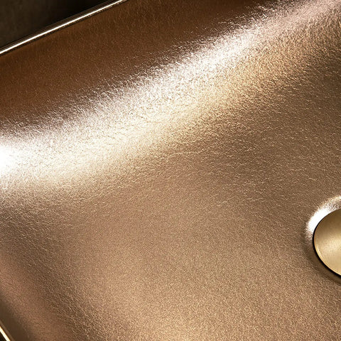 Close-up of gold plated rectangular bathroom vessel sink surface with a smooth finish and drain opening.