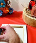 Person applying glue to attach magnets to a canvas on a table, near fall-themed decorations and orange fabric backdrop.