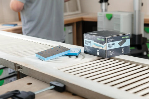 Foam Back Contouring Abrasive Discs with Hook and Loop Mount next to box, on a detailed wood surface in workshop.