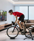 Cyclist using a Steel Bicycle Trainer Stand with Fluid Magnetic Resistance for Indoor Cycling, in a modern living room setup.