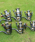 Set of six Smooth As Butter Spinning Fishing Reels with 11BB Bearing, 5.2:1 Gear, aluminum spool and CNC collapsible handle on grass.