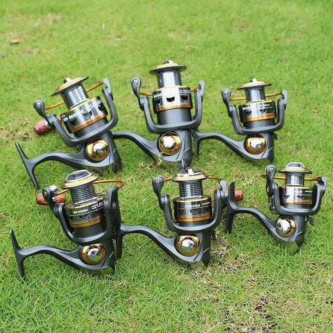 Set of six Smooth As Butter Spinning Fishing Reels with 11BB Bearing, 5.2:1 Gear, aluminum spool and CNC collapsible handle on grass.