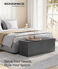 Mazie Collection 43 Inch Folding Storage Ottoman Bench With Quick Foldaway End Of Bed Foot Rest And Underbed Storage Go-To For Living Room Bedroom Or Entryway Dark Gray in bedroom setting.