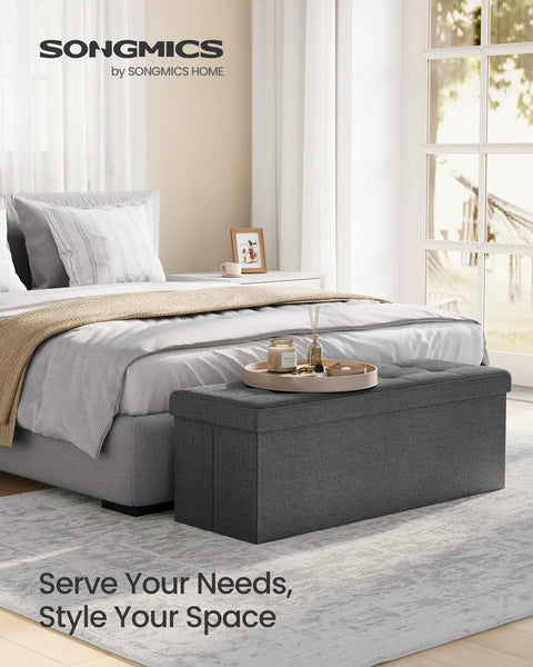 Mazie Collection 43 Inch Folding Storage Ottoman Bench With Quick Foldaway End Of Bed Foot Rest And Underbed Storage Go-To For Living Room Bedroom Or Entryway Dark Gray in bedroom setting.