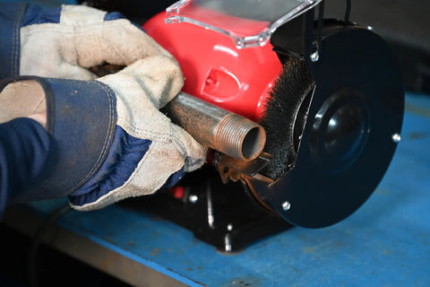 User operating a Six Inch Wide Face Bench Grinder Wire Wheel on a rusty metal pipe in a workshop.