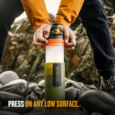 Close-up of hands pressing GeoPress 24 Oz Water Purifier Bottle for hiking and camping against rocks, showing easy fill press to drink design.