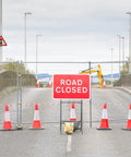 Outdoor scene with a road closed sign, metal barrier, and orange cones for crowd control at a construction site