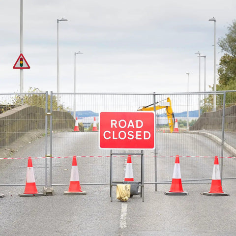Outdoor scene with a road closed sign, metal barrier, and orange cones for crowd control at a construction site