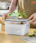 Person handling clear container from 4 Pack Fridge Fruit Storage Containers With Removable Colanders, Airtight Food Saver on a kitchen counter