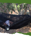 Man sleeping in Bug Free Sky Bed Camping Hammock Tent With Flat Lay Sleep under trees, showcasing asymmetrical design and pad sleeve.