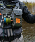 Angler wearing Stormshadow Fly Fishing Chest Pack with Waterproof Pocket, Velcro Fly Patch, and Tool Attachment Points by a river.