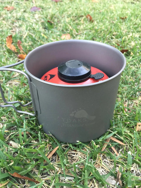 Ultralight Titanium 550ml Pot With Lid For Backpacking And Camping on grass with stove gear visible inside