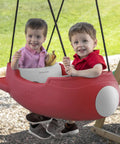 Rocket Swing For Two Outdoor Baby Swing With Weather Resistant Rope Attaches To Your Playset In The Backyard For Toddlers 9 Months To 3 Years Old Safe Buckle Comfort And Easy No Fuss Setup For Kid Friendly Fun; Two toddlers in red rocket-shaped swing on playset outdoors.