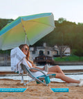 Person relaxing on High Back Beach Chair With Umbrella And Cooler Cup Holder And Carry Bag at beach, featuring a cup holder.