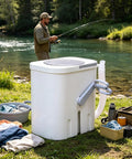Portable Manual Crank Washing Machine Cordless Laundry Setup Eight Liter Capacity Power Free Operation For Camp Sites Dorm Rooms And Weekend Outings A Game Changer For Fresh Thread Care beside a man fishing by a river, with laundry nearby.