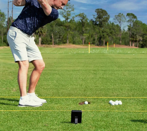 Golfer practicing on grass using LM1 Portable Mini Launch Monitor For Golfers With Real Time Ball And Club Speed Tracking Smash Factor Stats
