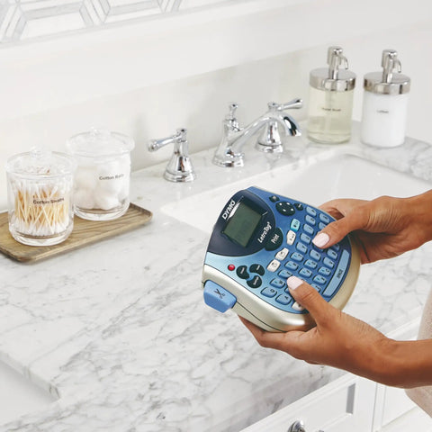 Person using Portable Handheld Label Maker With QWERTY Keyboard And 2 Line Printing on a marble bathroom counter.