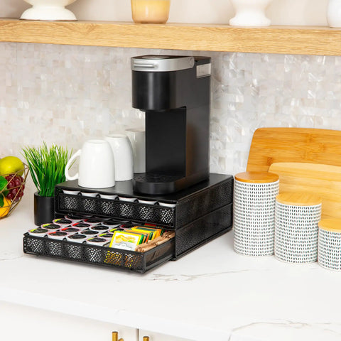 Two Drawer Coffee Pod Organizer With Removable Dividers Fits Up To 72 Pods Or Mix Of Pods And Office Essentials, Metal Mesh Coffee Station Base With Guided Drawer Track For Smooth Opening, Black Finish in kitchen setting with coffee maker and cups on top.