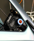 Juin F1-S black hydraulic disc brake caliper mounted on bicycle frame with blue adjustment knob
