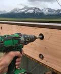 Person using Hammer Drill With Brushless Motor, Tool Only No Battery, 36V MultiVolt on wood beam outdoors with mountain view.