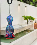 Outdoor Hand Blown Glass Hummingbird Feeder With 24 Oz Capacity And Four Feeding Ports hanging in a garden setting