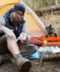 Man using 380 Piece Deluxe First Aid Kit With Bandages Gauze Rolls Instant Cold Packs And Emergency Blanket Compact Orange Kit for outdoor care next to a tent.