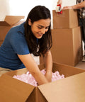 Person packing pink packing peanuts for shipping and moving, 14 cubic feet antistatic void fill cushioning supplies in box.