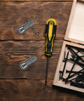 Flatlay of a yellow and black screwdriver, screws, and metal clips on a wooden table next to a wooden box.