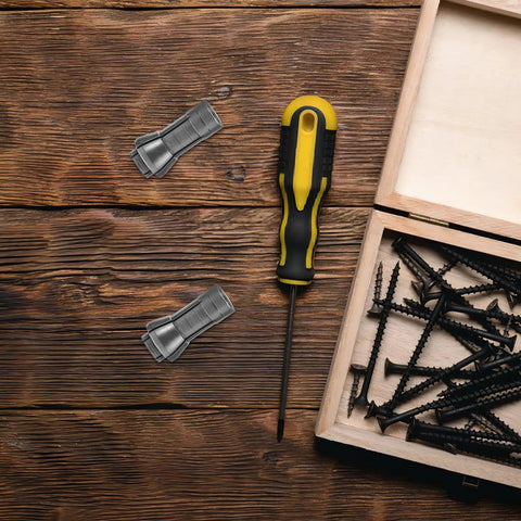 Flatlay of a yellow and black screwdriver, screws, and metal clips on a wooden table next to a wooden box.