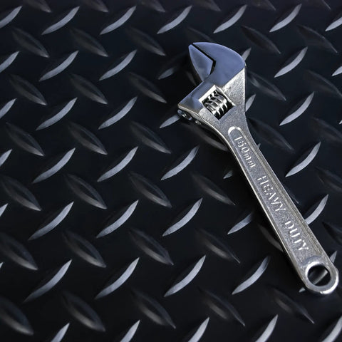 Heavy Duty Vinyl Diamond Plate Floor Mat Non Slip Garage Flooring Chemical Resistant One Eighth Inch Thick By Twenty Four Wide By Eight Feet Long Black With Yellow Border with a shiny adjustable wrench on top.