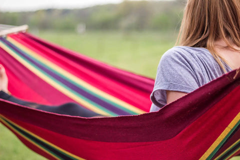 Person relaxing in a Cotton Blend Bahamas Hammock In Burgundy With Caribbean Colors Soft Cotton Fabric Hardwood Spreader Bars Braided Attachment Rope