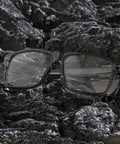 Real Deal Job Site Safety Glasses With Smash Proof Polycarbonate Lenses laying on dark rocky surface, showcasing the anti-fog design.