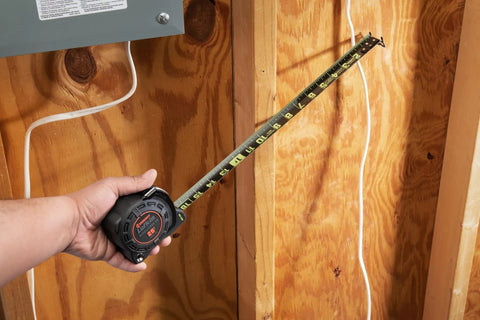 Hand using Auto Lock Tape Measure With 25 Foot Reach, Thick Diamond Coated Blade against wooden panel