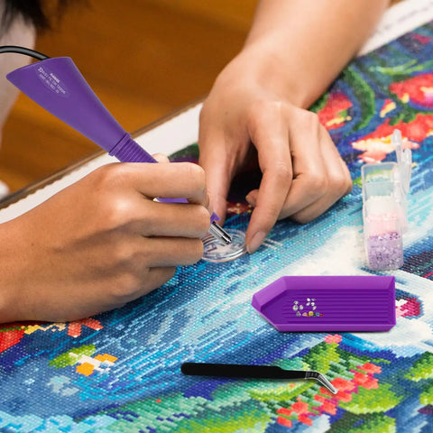 Hotfix Rhinestone Setter Kit With 7 Tips And Quick Heat Wand Diamond Bowl Stand Tweezers Cleaning Brush Wax Pens And 3 Boxes Of Colorful Crystals For DIY Embellishments And Jewelry Making Purple being used on a craft project.