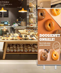 Bakery setting with a custom retractable banner with aluminum stand promoting doughnut sale, 33x81 inches, in full color design.