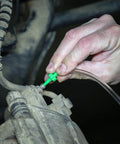 Hand attaching a bright green brake bleeder adapter to a dusty car brake caliper using a clear hose