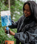 Person using Portable Squeeze Water Filtration System with Two 32 Oz Pouches, Straw, and Hydration Pack Adapter outdoors