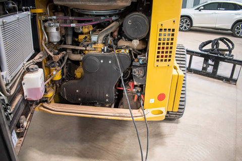 Construction vehicle engine with cables attached. Heavy Duty Battery Booster Cables 16 Feet With 500 Amp Clamps visible.