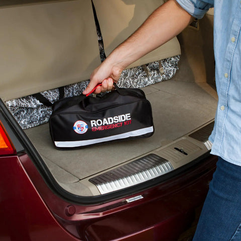 Person placing 125 Piece Roadside Emergency Kit For Cars With Headlamp First Aid Tools And Visibility Gear in vehicle trunk.